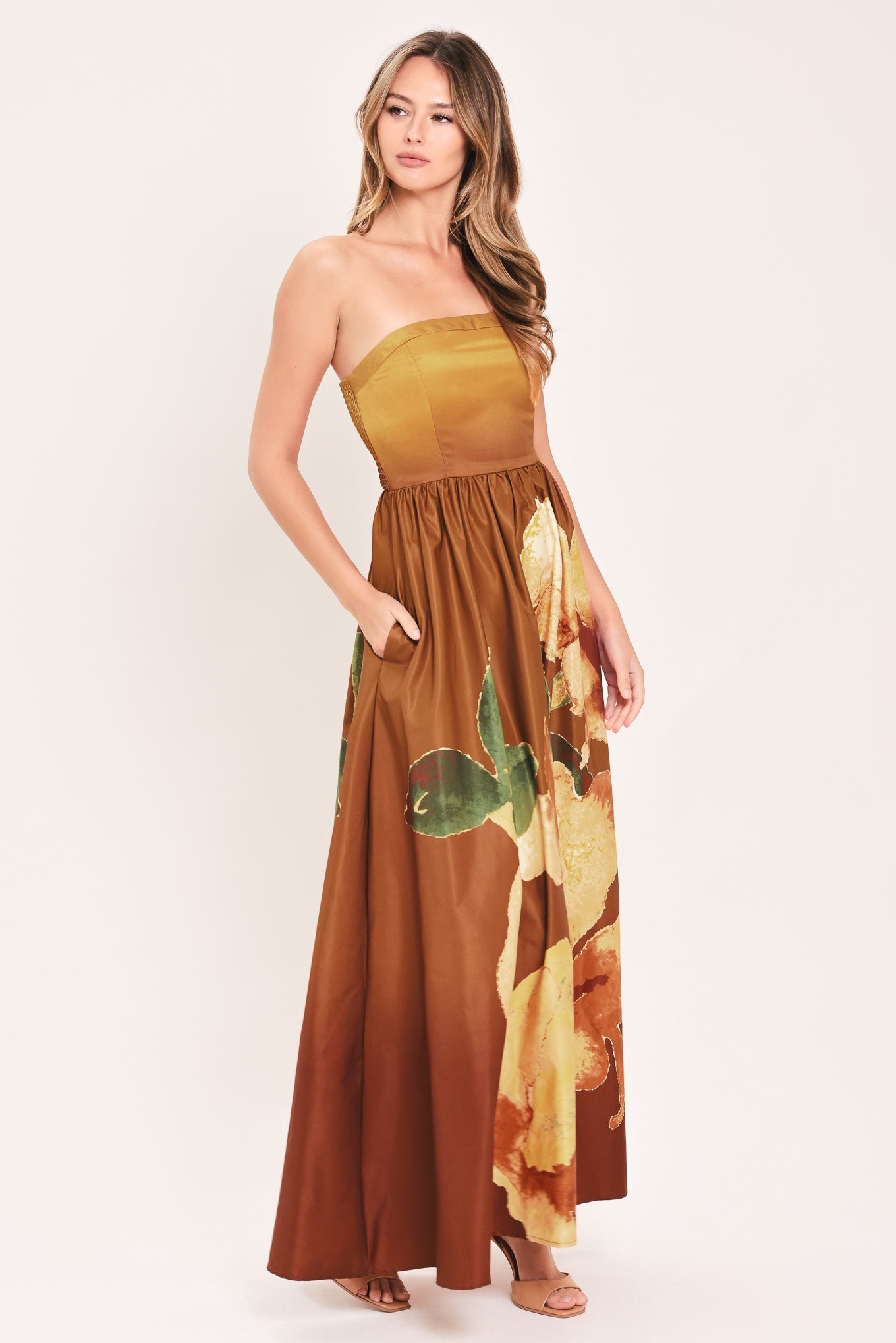 A woman modeling a strapless maxi dress with a mustard yellow bodice and a brown skirt featuring a large yellow floral print with green leaves | Flying Tomato