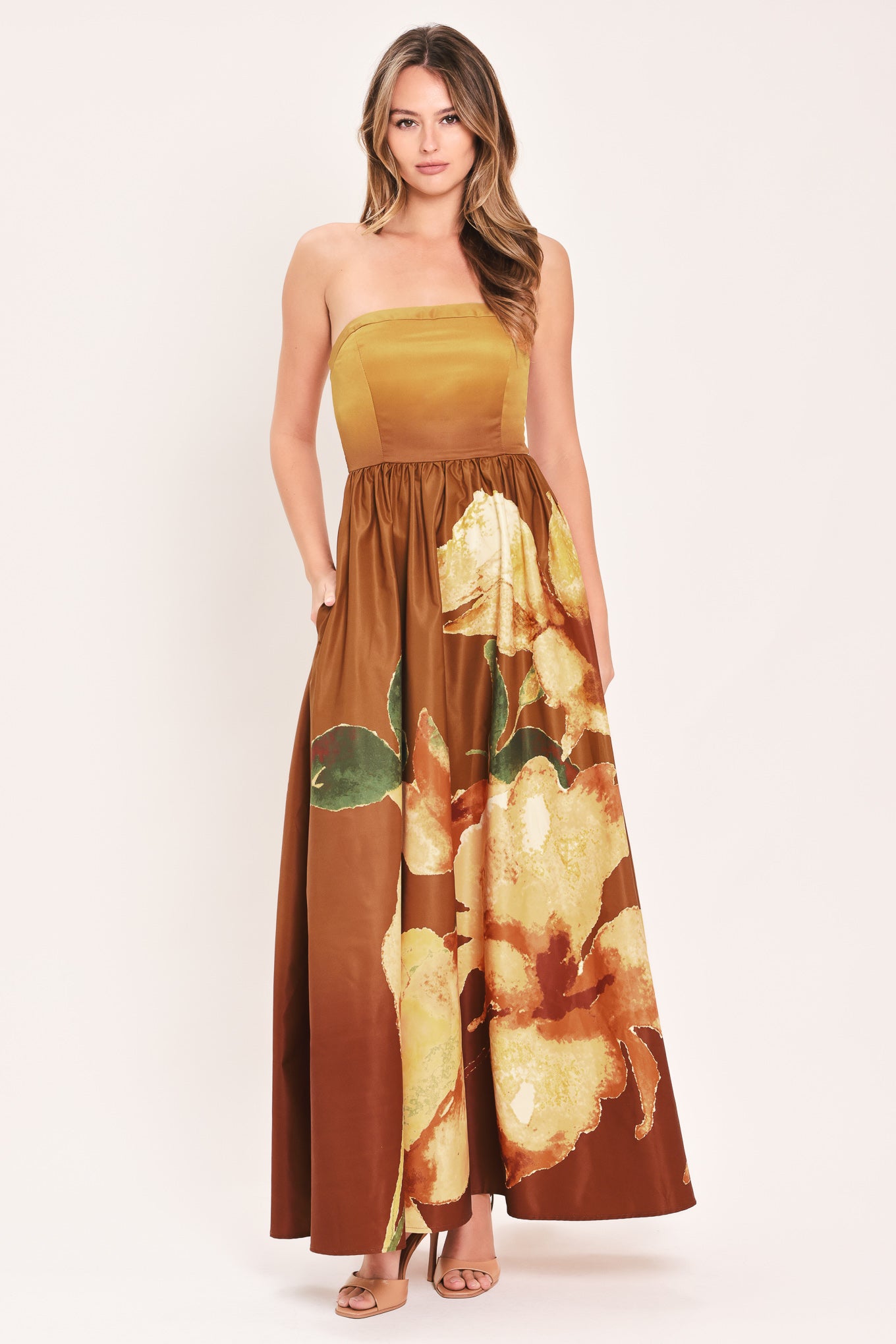 A woman modeling a strapless maxi dress with a mustard yellow bodice and a brown skirt featuring a large yellow floral print with green leaves | Flying Tomato