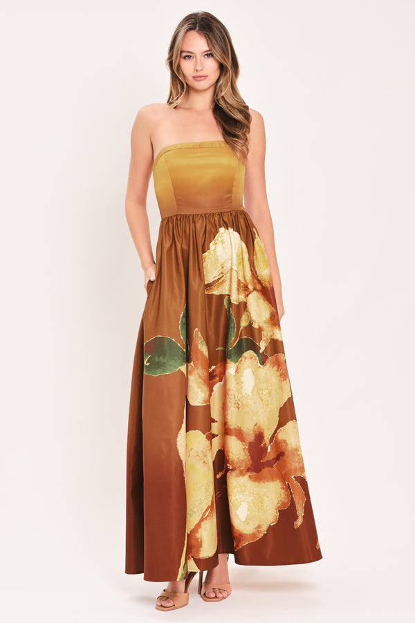 A woman modeling a strapless maxi dress with a mustard yellow bodice and a brown skirt featuring a large yellow floral print with green leaves | Flying Tomato