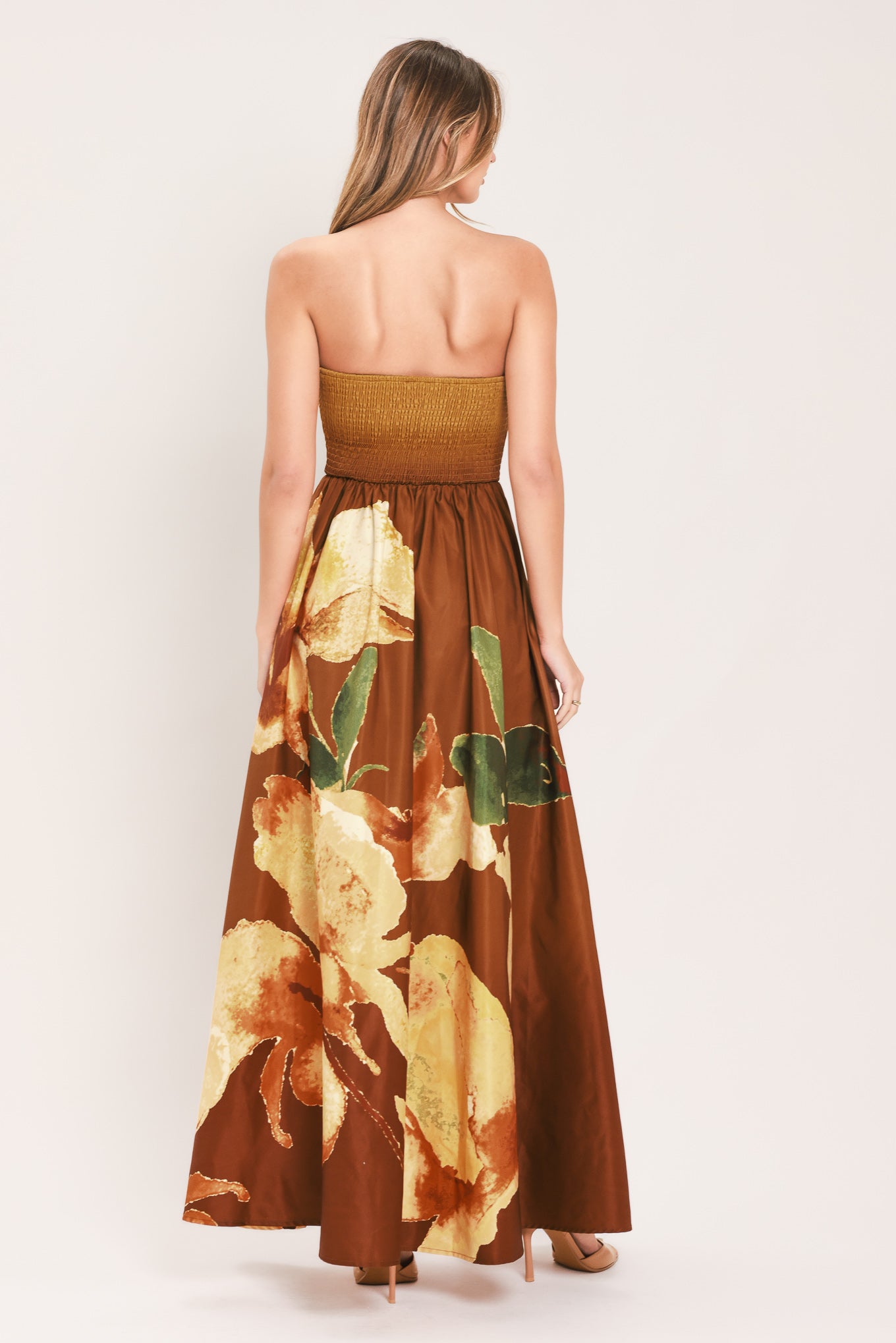 A woman modeling a strapless maxi dress with a mustard yellow bodice and a brown skirt featuring a large yellow floral print with green leaves | Flying Tomato