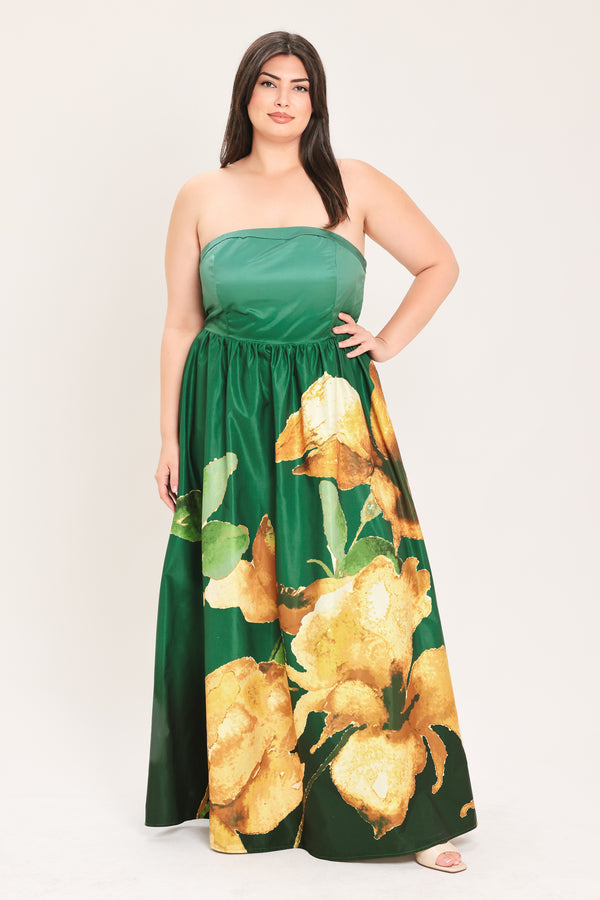 A woman modeling a strapless maxi dress with a green satin-like bodice and a large yellow floral print on a dark green skirt, photographed against a plain light background.