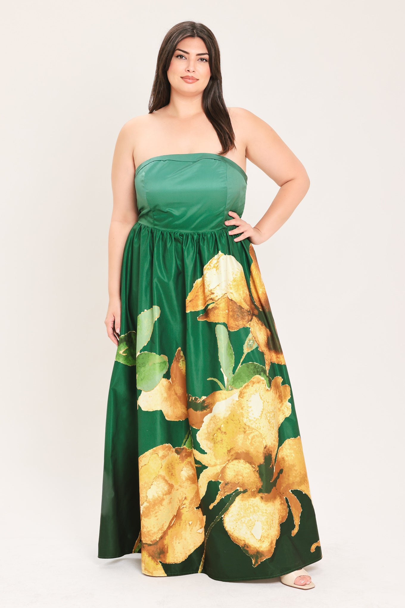 A woman modeling a strapless maxi dress with a green satin-like bodice and a large yellow floral print on a dark green skirt | Flying Tomato Curve