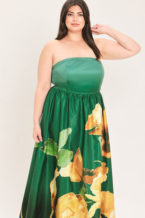 A woman modeling a strapless green maxi dress with a large gold and green floral print on the skirt, set against a plain light background.