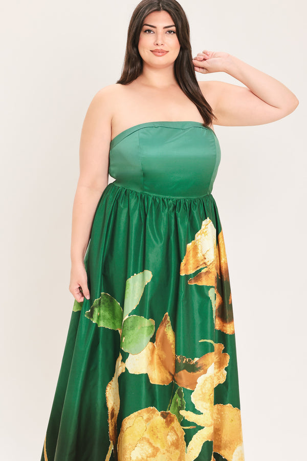 A woman modeling a strapless green maxi dress with a large gold and green floral print on the skirt, set against a plain light background.
