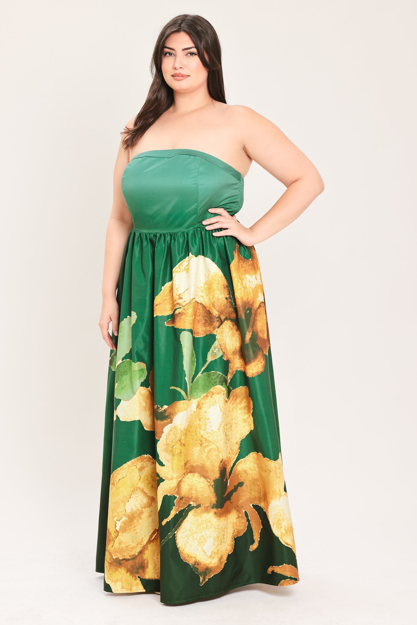A woman modeling a strapless maxi dress with a green satin-like bodice and a large yellow floral print on a dark green skirt | Flying Tomato Curve