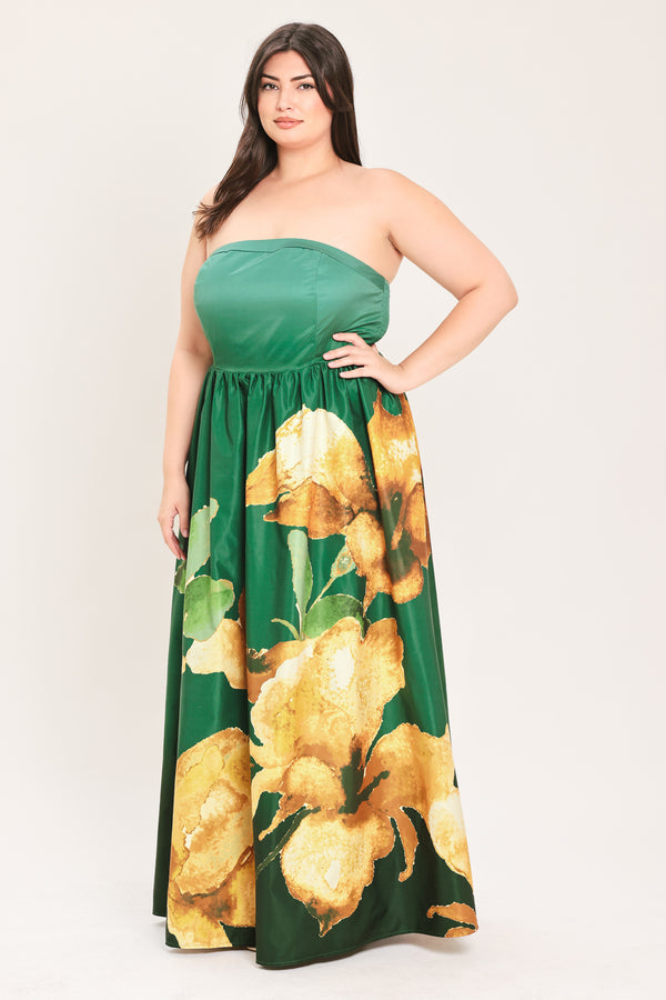 A woman modeling a strapless green maxi dress with a large gold floral print on the skirt, posed against a plain light background.