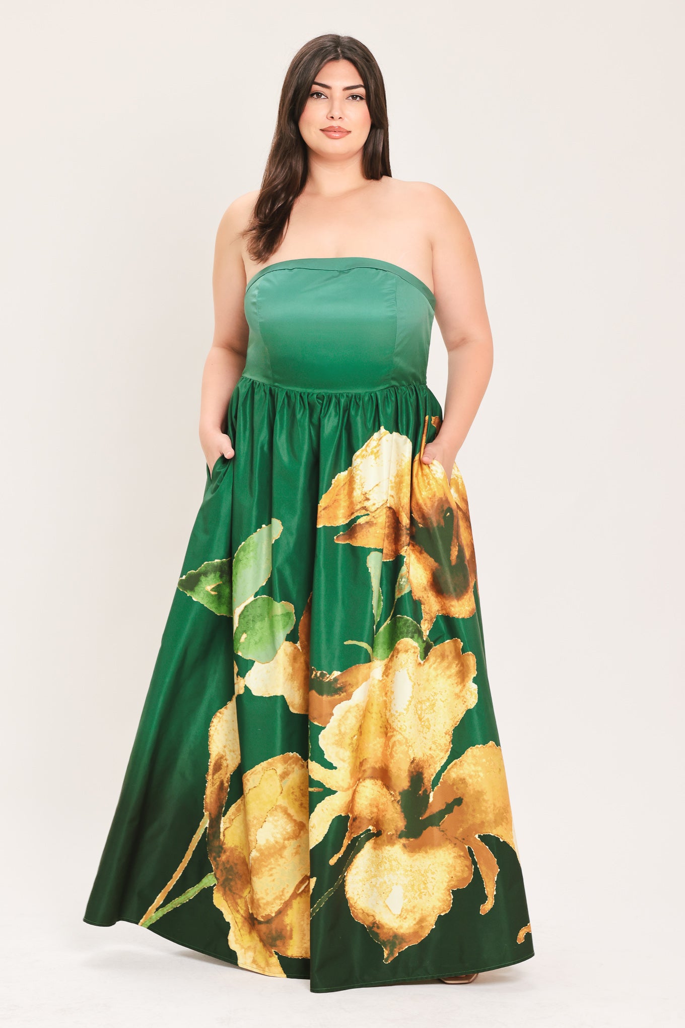 A woman modeling a strapless maxi dress with a green satin-like bodice and a large yellow floral print on a dark green skirt | Flying Tomato Curve