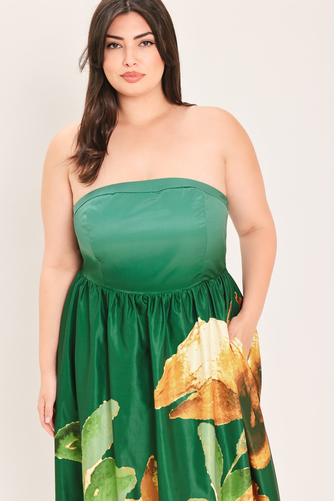 A woman modeling a strapless maxi dress with a green satin-like bodice and a large yellow floral print on a dark green skirt | Flying Tomato Curve