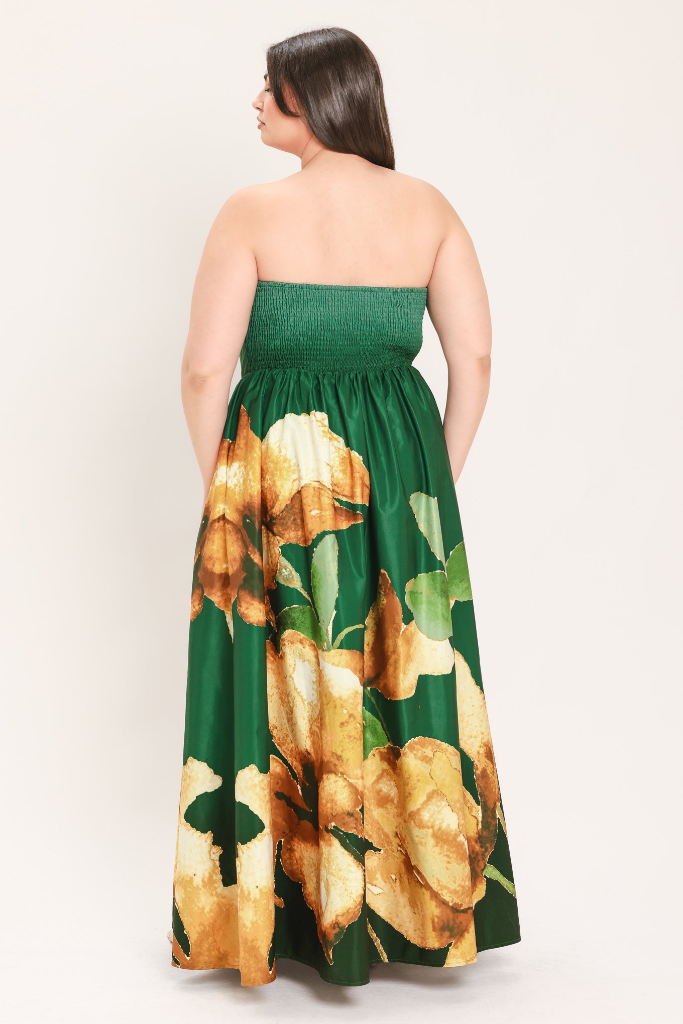 A woman modeling a strapless maxi dress with a green satin-like bodice and a large yellow floral print on a dark green skirt | Flying Tomato Curve
