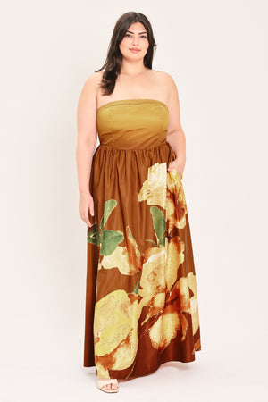 A woman modeling a strapless dress with a mustard yellow bandeau-style bodice and a brown skirt featuring a large green and gold floral print, set against a plain light background.