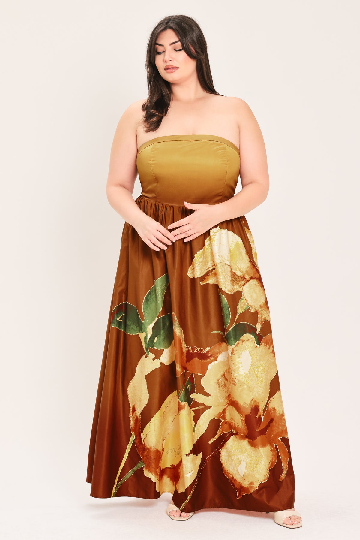 A woman modeling a strapless dress with a mustard yellow bandeau-style bodice and a brown skirt featuring a large green and gold floral print, set against a plain light background.