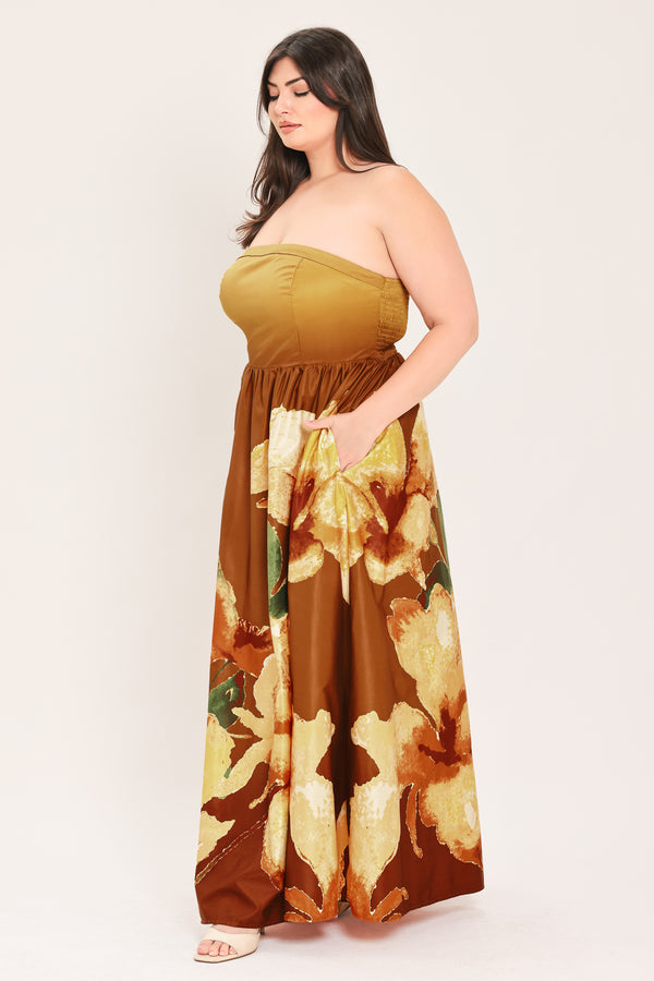 A woman modeling a strapless dress with a mustard yellow bandeau-style bodice and a brown skirt featuring a large green and gold floral print, set against a plain light background.