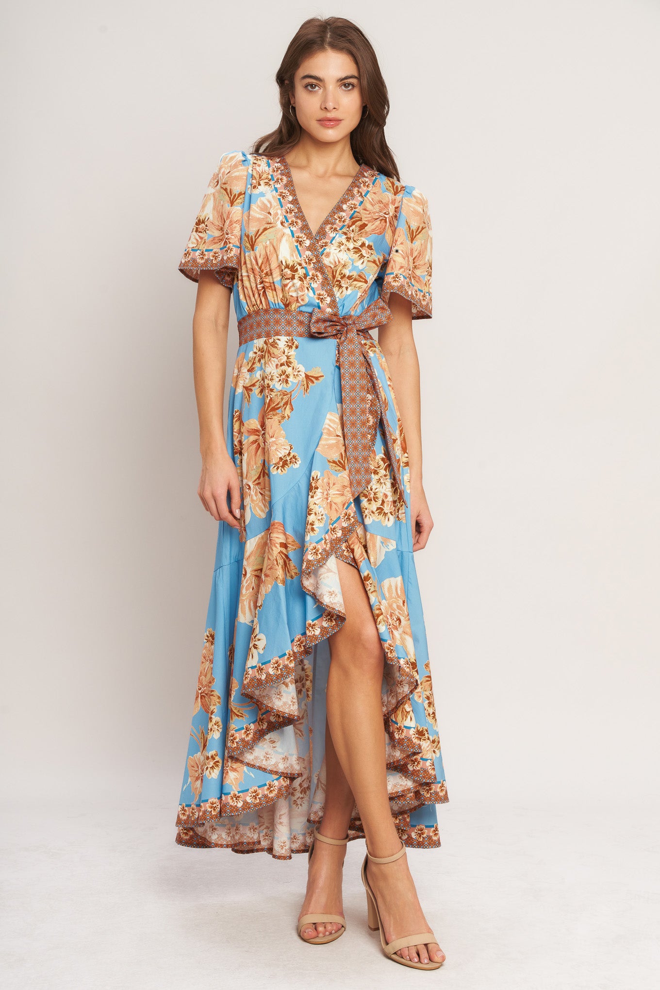 A printed woven hi-lo midi dress featuring surplice neckline, short flutter sleeve, side tie, ruffle hem and smocked back waistband