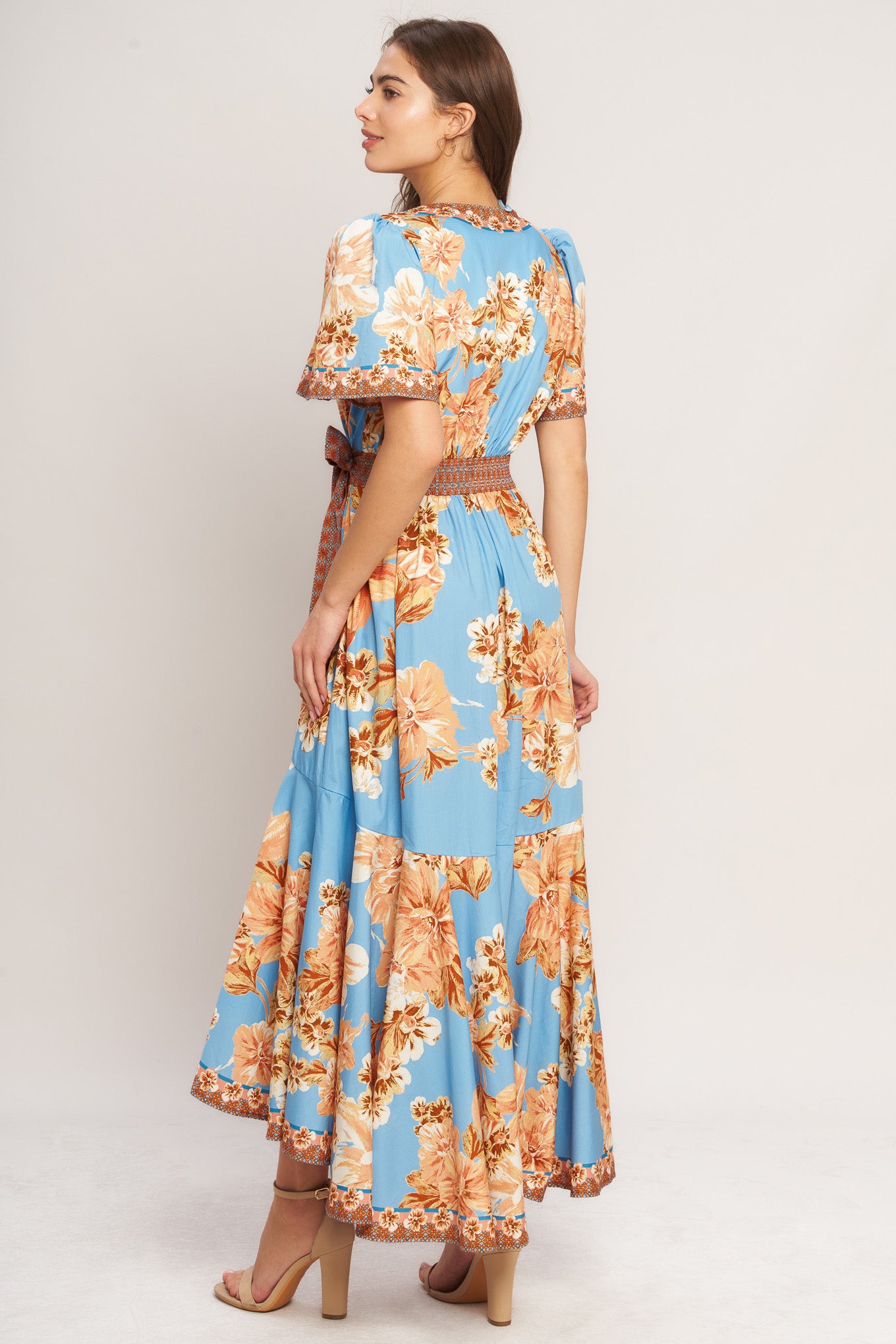 A printed woven hi-lo midi dress featuring surplice neckline, short flutter sleeve, side tie, ruffle hem and smocked back waistband