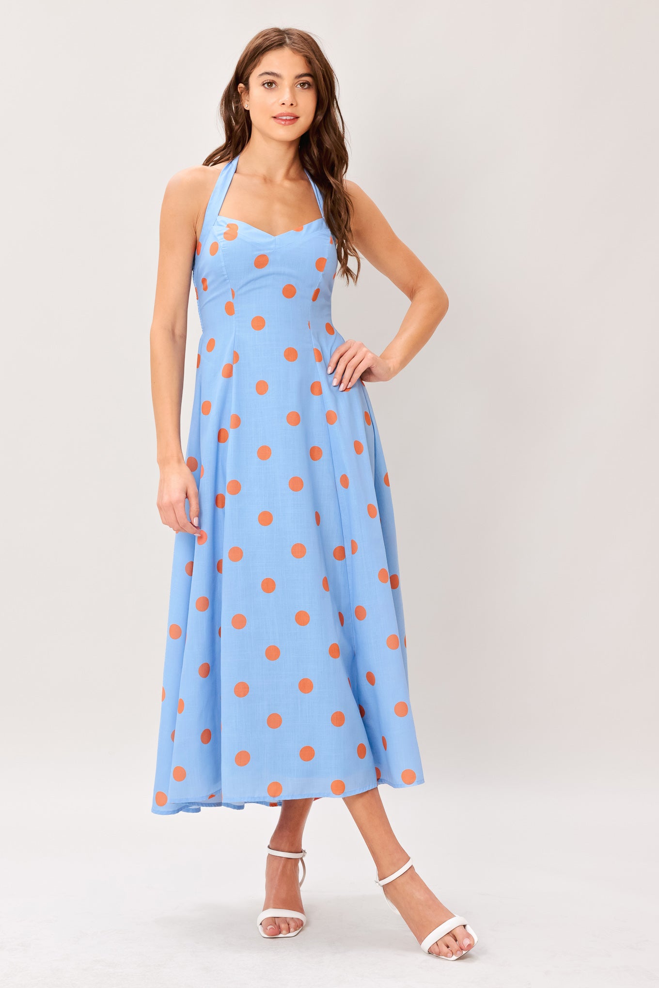 Woman wearing a blue with orange polka dots printed woven midi dress featuring sweetheart neckline, halter tie, full skirt and smocked back bodice 
