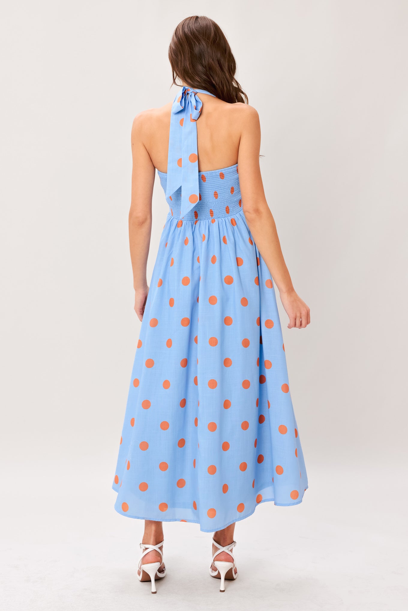 Woman wearing a blue with orange polka dots printed woven midi dress featuring sweetheart neckline, halter tie, full skirt and smocked back bodice 