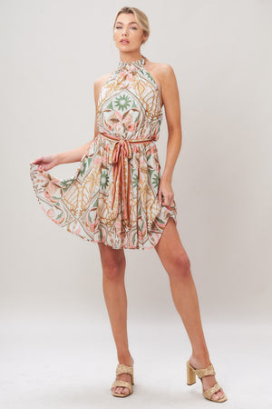 Woman wearing a printed woven mini dress featuring halter neckline, elastic waist with self sash, full skirt, bare back with tie on a white background | Flying Tomato