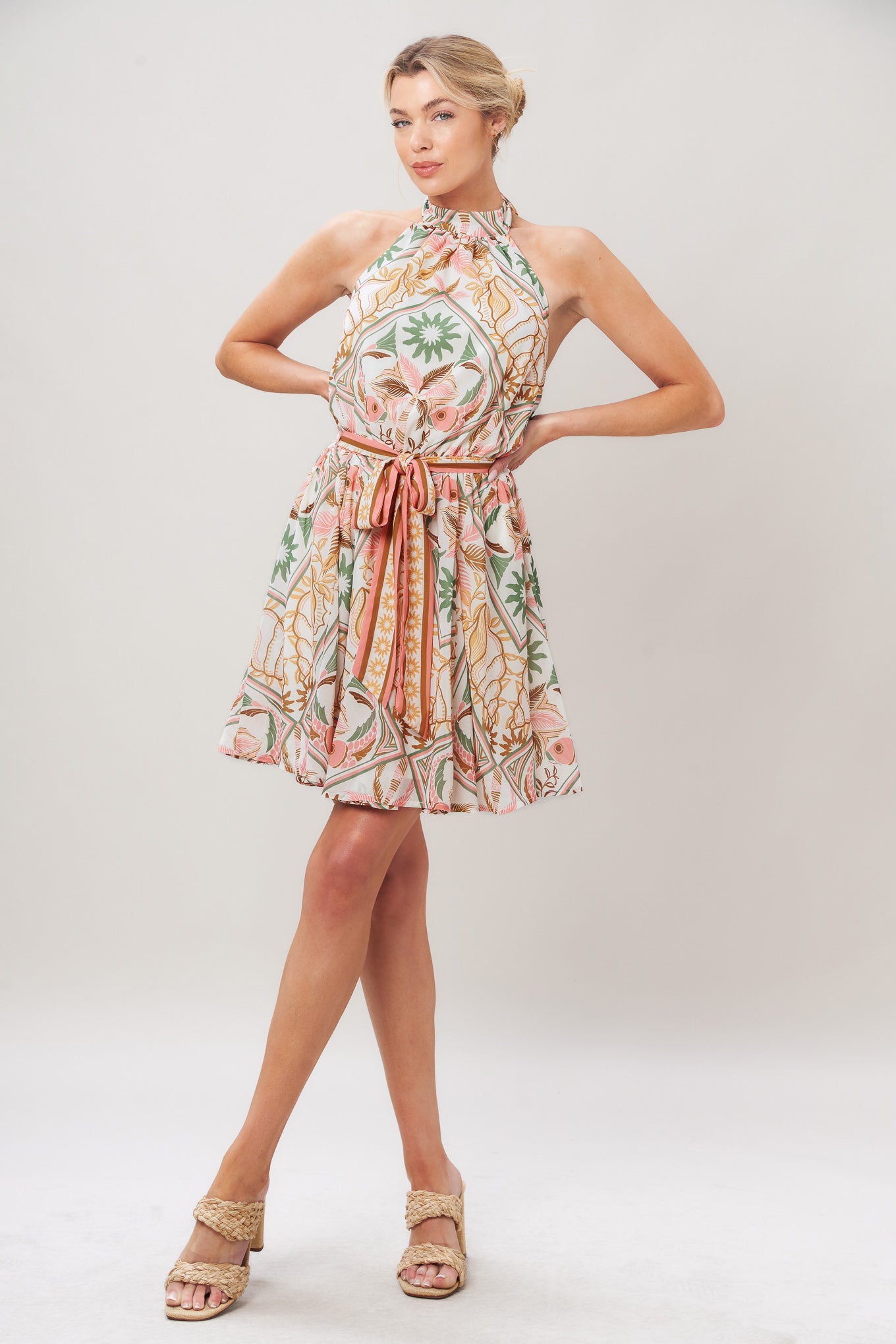 Woman wearing a printed woven mini dress featuring halter neckline, elastic waist with self sash, full skirt, bare back with tie on a white background | Flying Tomato