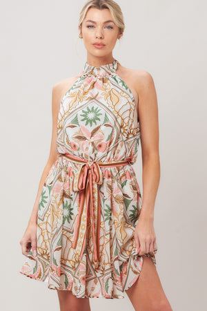 Woman wearing a printed woven mini dress featuring halter neckline, elastic waist with self sash, full skirt, bare back with tie on a white background | Flying Tomato