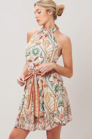 Woman wearing a printed woven mini dress featuring halter neckline, elastic waist with self sash, full skirt, bare back with tie on a white background | Flying Tomato