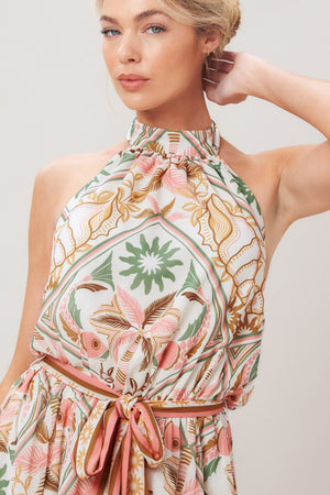 Woman wearing a printed woven mini dress featuring halter neckline, elastic waist with self sash, full skirt, bare back with tie on a white background | Flying Tomato
