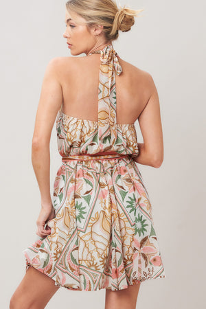Woman wearing a printed woven mini dress featuring halter neckline, elastic waist with self sash, full skirt, bare back with tie on a white background | Flying Tomato