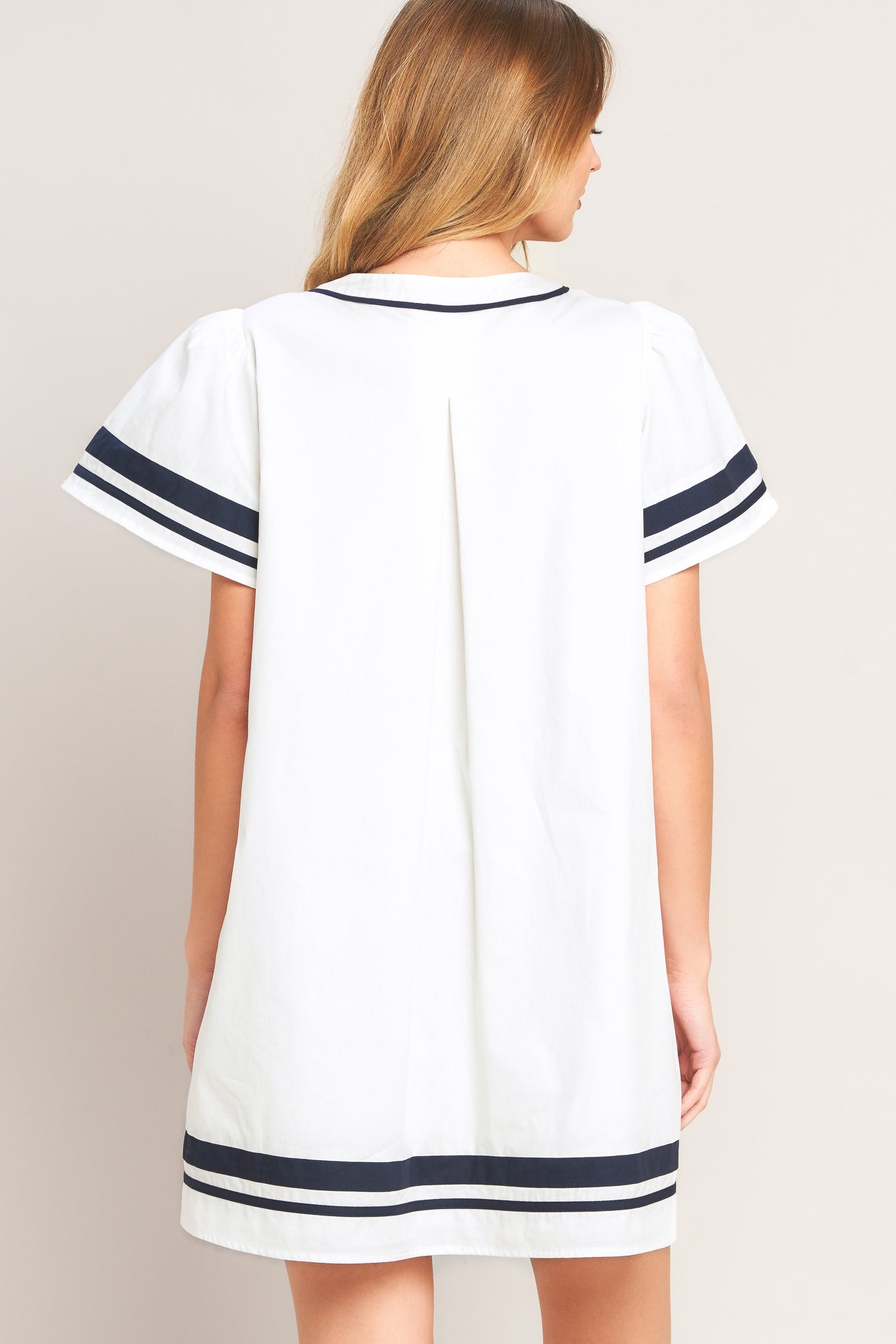 White dress with navy trim worn by a model on a plain background