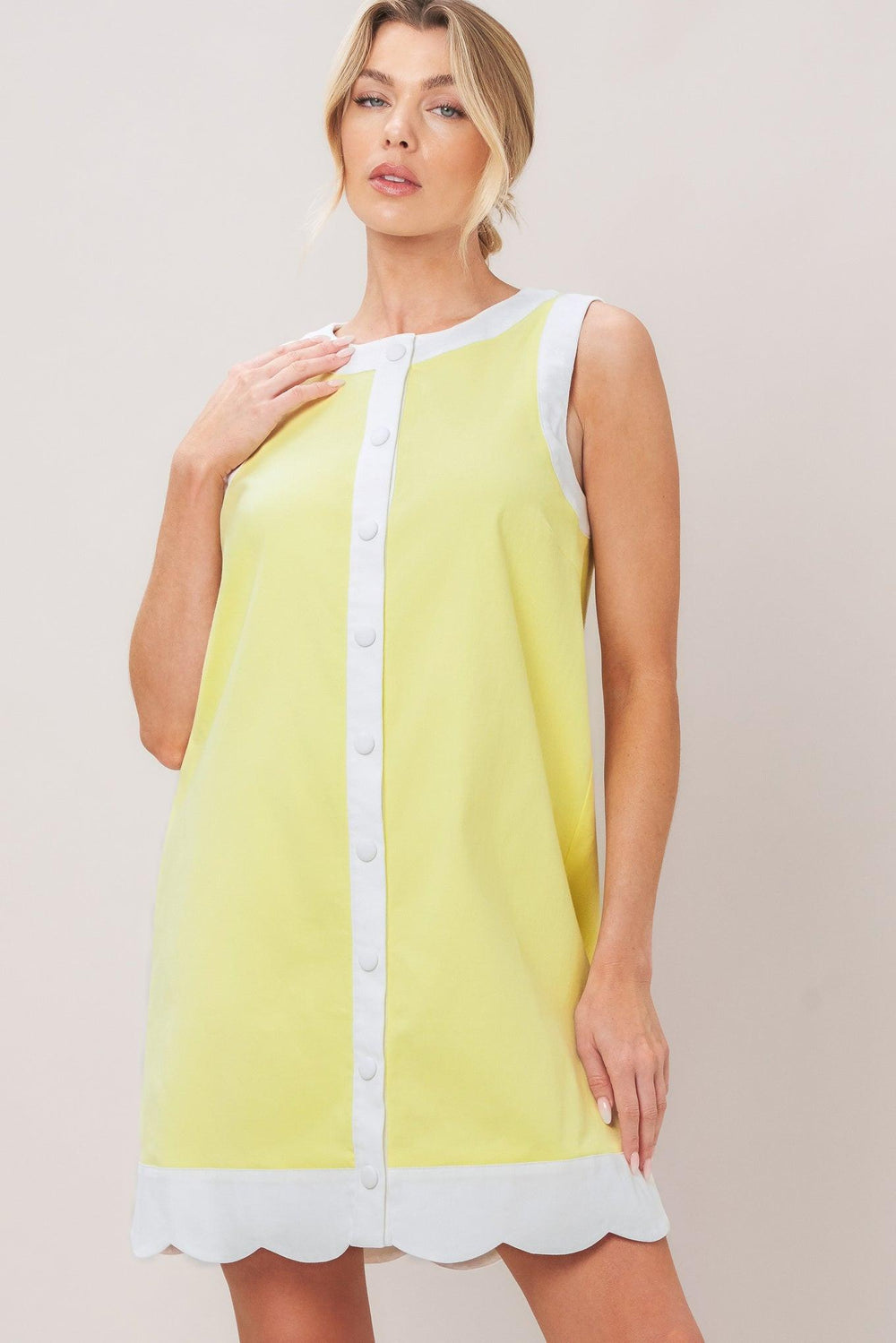 Woman wearing a pink with white trim mini dress featuring round neckline, sleeveless, front button down and scallop hem