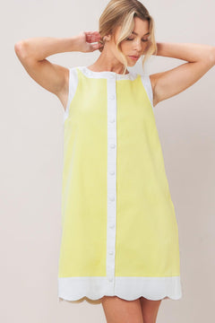 Woman wearing a yellow with white trim mini dress featuring round neckline, sleeveless, front button down and scallop hem