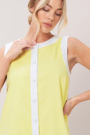 Woman wearing a yellow with white trim mini dress featuring round neckline, sleeveless, front button down and scallop hem