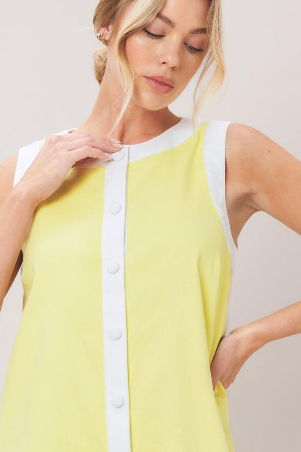 Woman wearing a yellow with white trim mini dress featuring round neckline, sleeveless, front button down and scallop hem