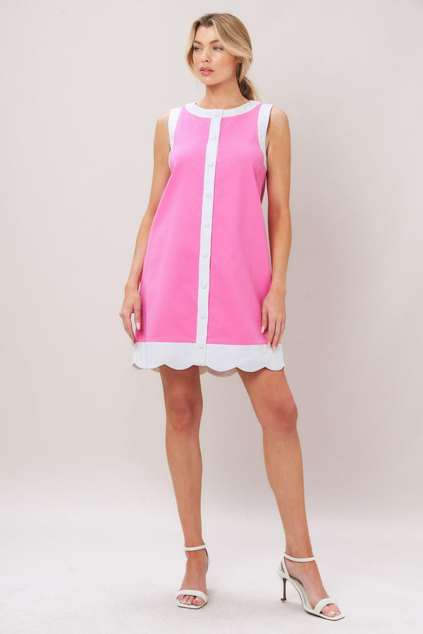 Woman wearing a pink with white trim mini dress featuring round neckline, sleeveless, front button down and scallop hem
