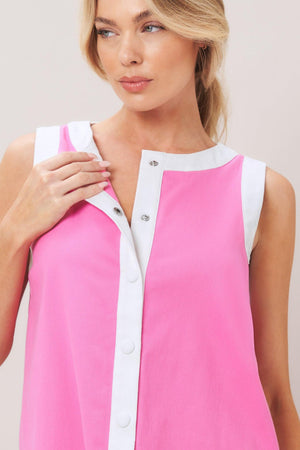 Woman wearing a pink with white trim mini dress featuring round neckline, sleeveless, front button down and scallop hem