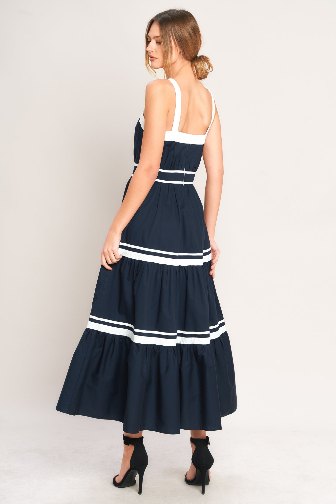 Woman wearing a navy dress with white stripes on a plain background