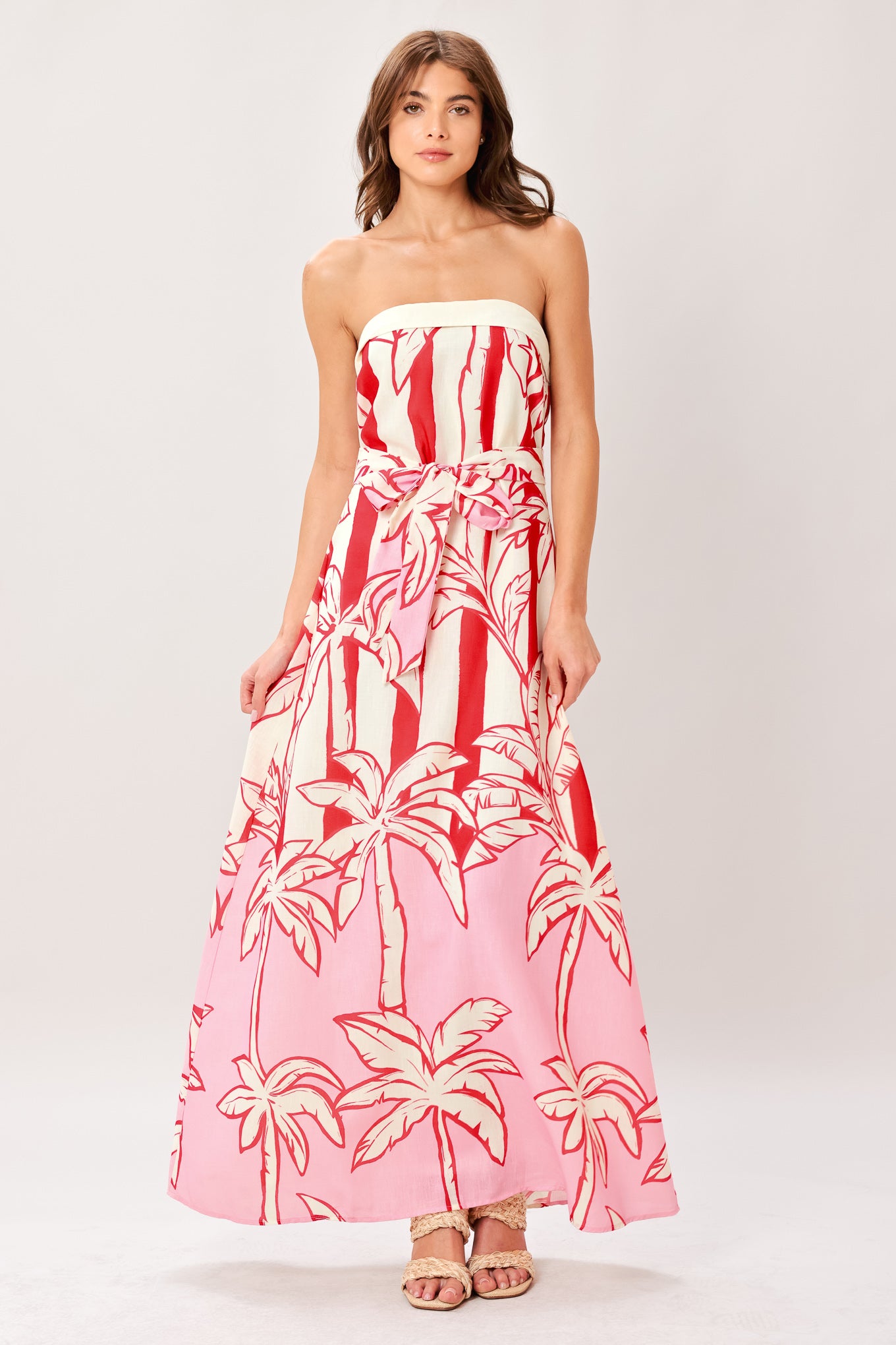 Woman wearing a red and white palm tree pattern printed woven ankle dress featuring strapless, front fold, self sash and back zipper closure