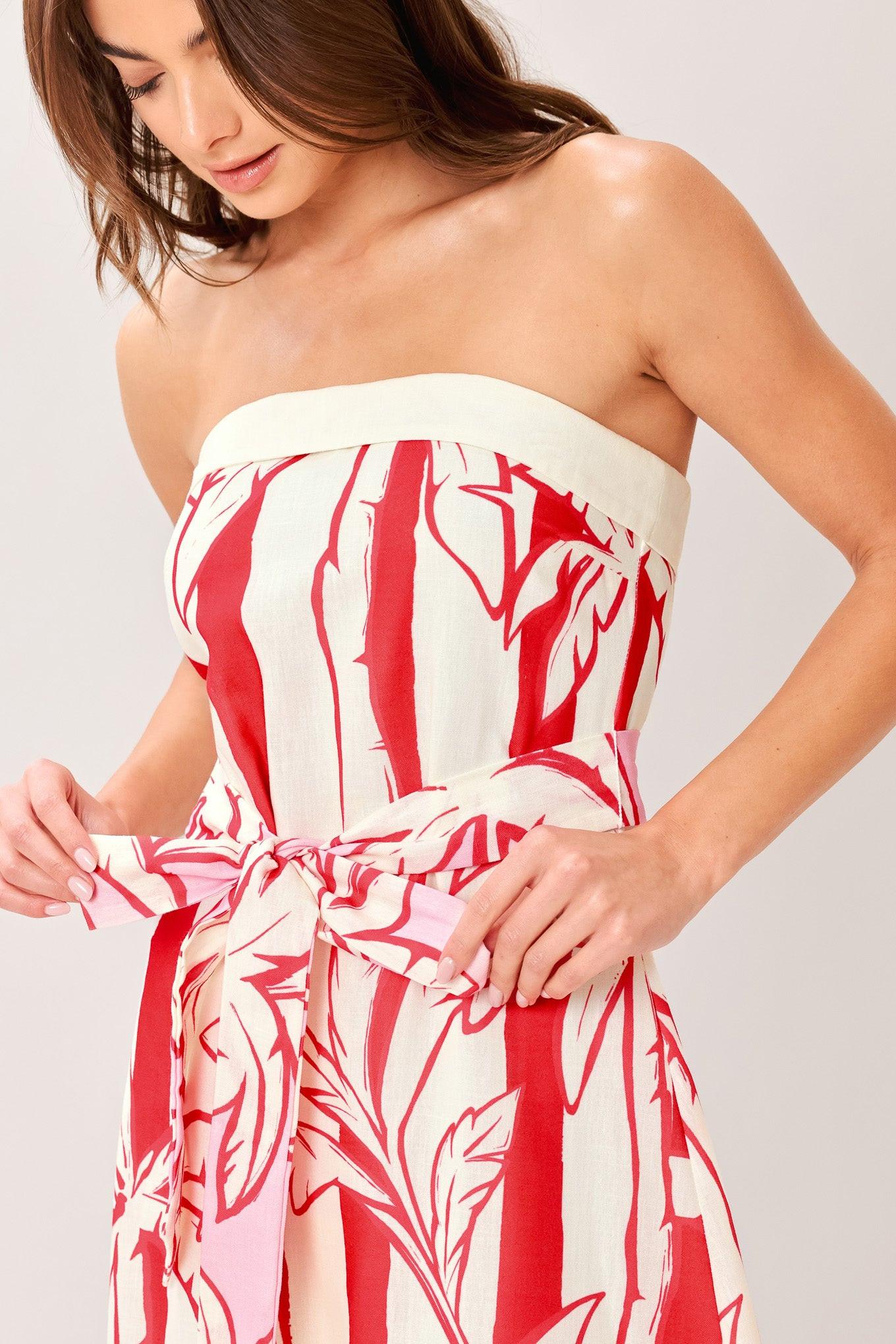 Woman wearing a red and white palm tree pattern printed woven ankle dress featuring strapless, front fold, self sash and back zipper closure