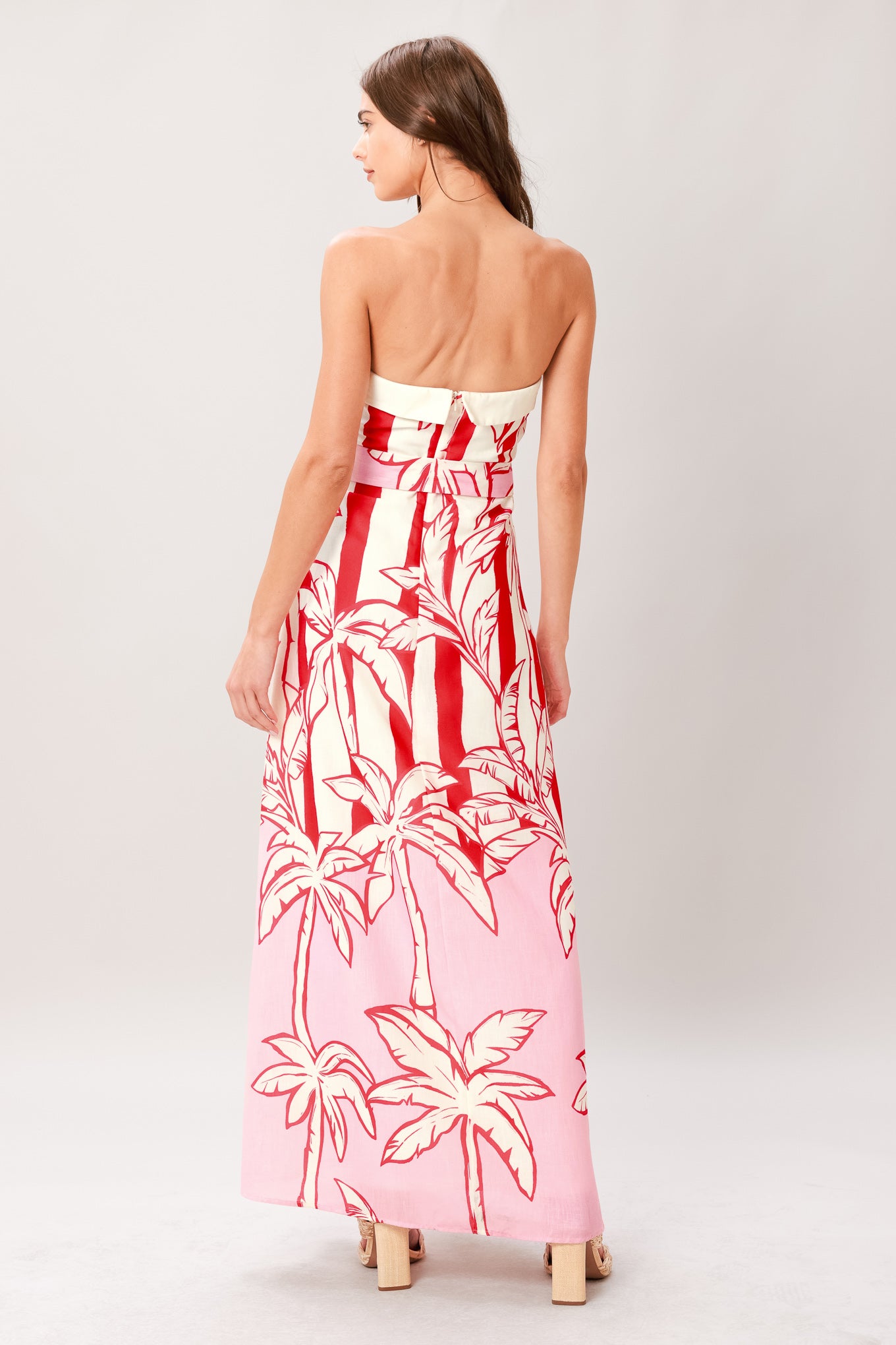 Woman wearing a red and white palm tree pattern printed woven ankle dress featuring strapless, front fold, self sash and back zipper closure