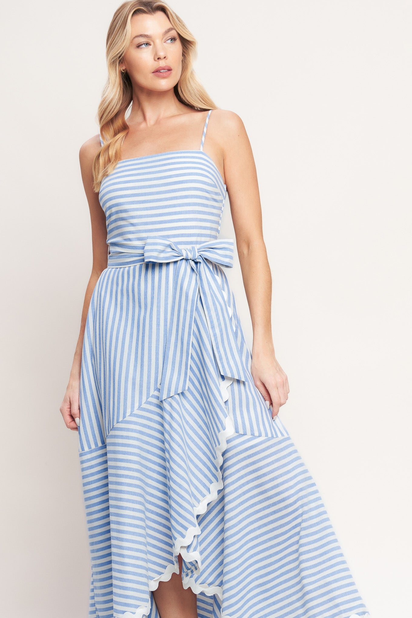 Blue-and-white striped midi dress with delicate straps, a waist bow tie, and a ruffled high-low hem

Details:

Self: 100% Cotton
Lining: 100% Polyester Exclusive of Decoration

Size & Fit

- Model is 5`8" And Wearing Size Small
- Measurements Taken From Size Small
- Approx. Length: 53"