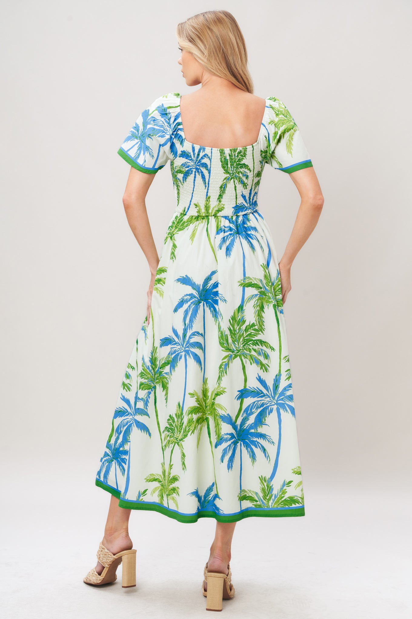 Woman wearing a tropical patterned dress featuring U neckline, short flutter sleeve, smocked bodice and full skirt on a white background | Flying Tomato