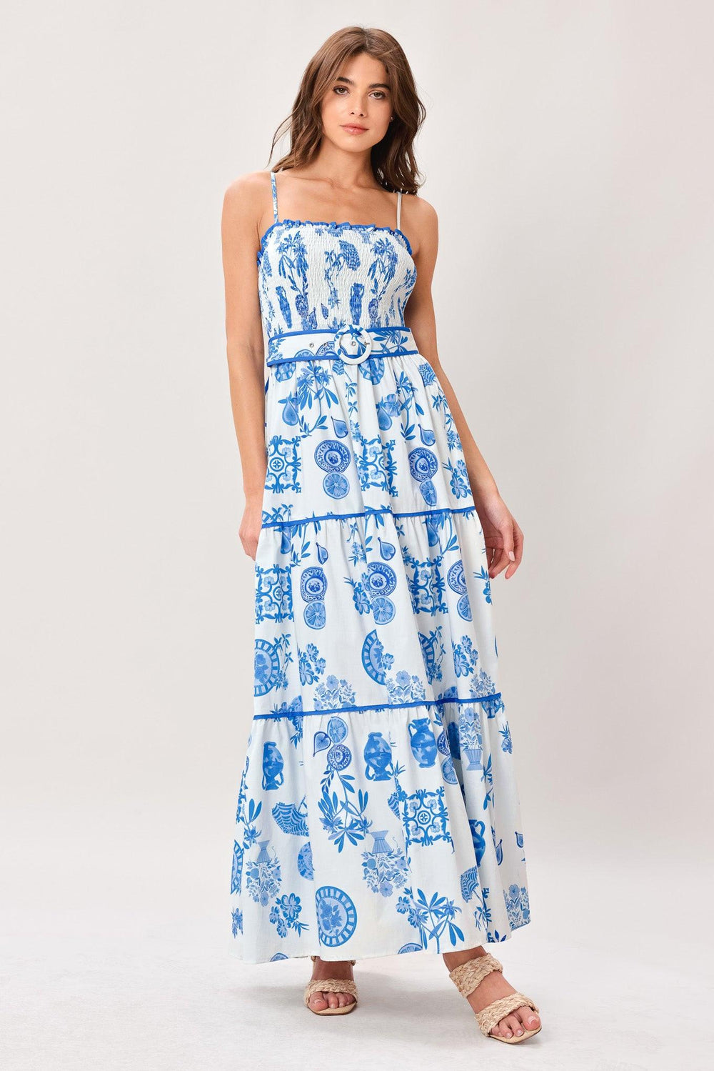 Woman wearing a blue and white patterned printed woven maxi dress featuring smocked bodice, straps, self belt and tier skirt