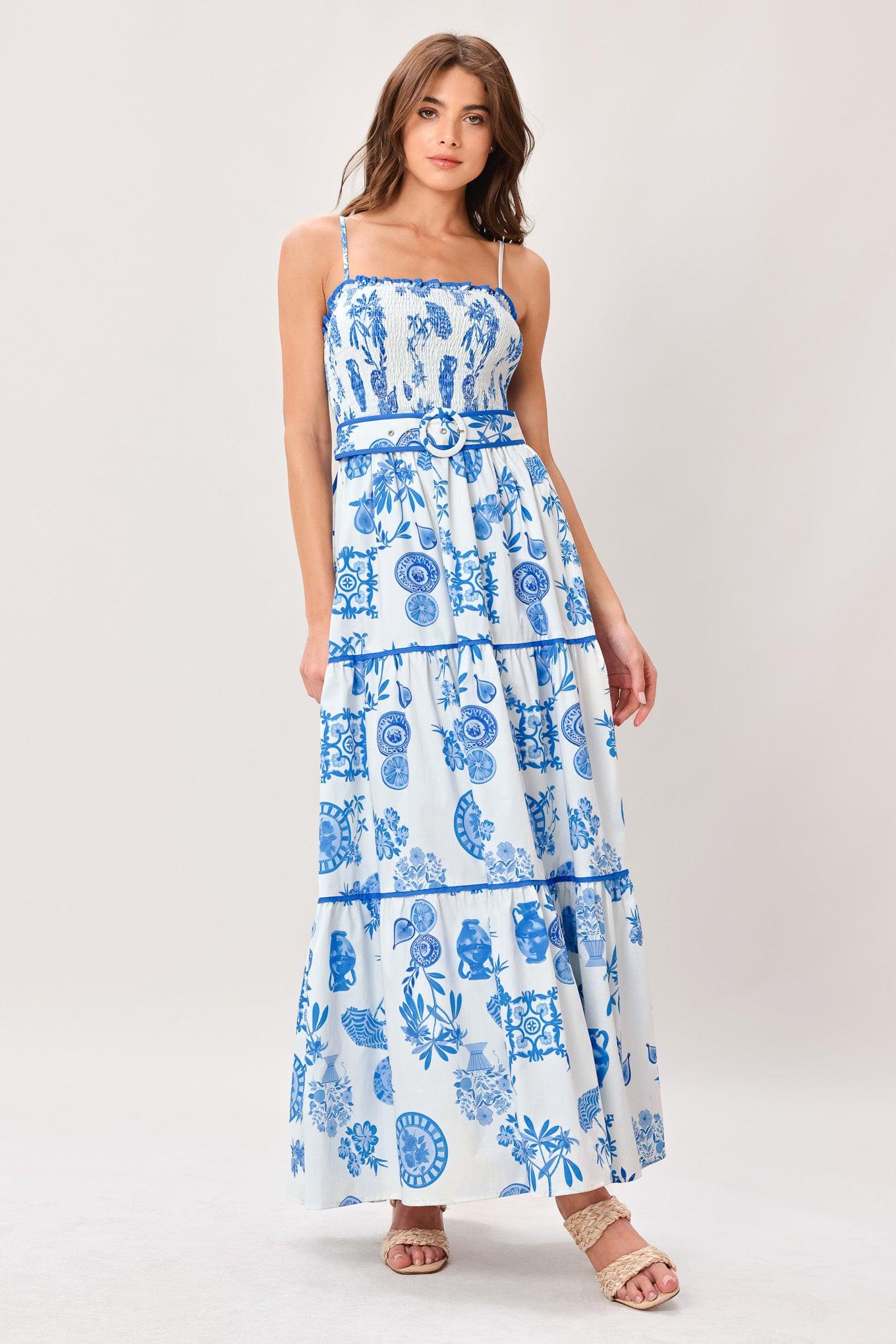 Woman wearing a blue and white patterned printed woven maxi dress featuring smocked bodice, straps, self belt and tier skirt