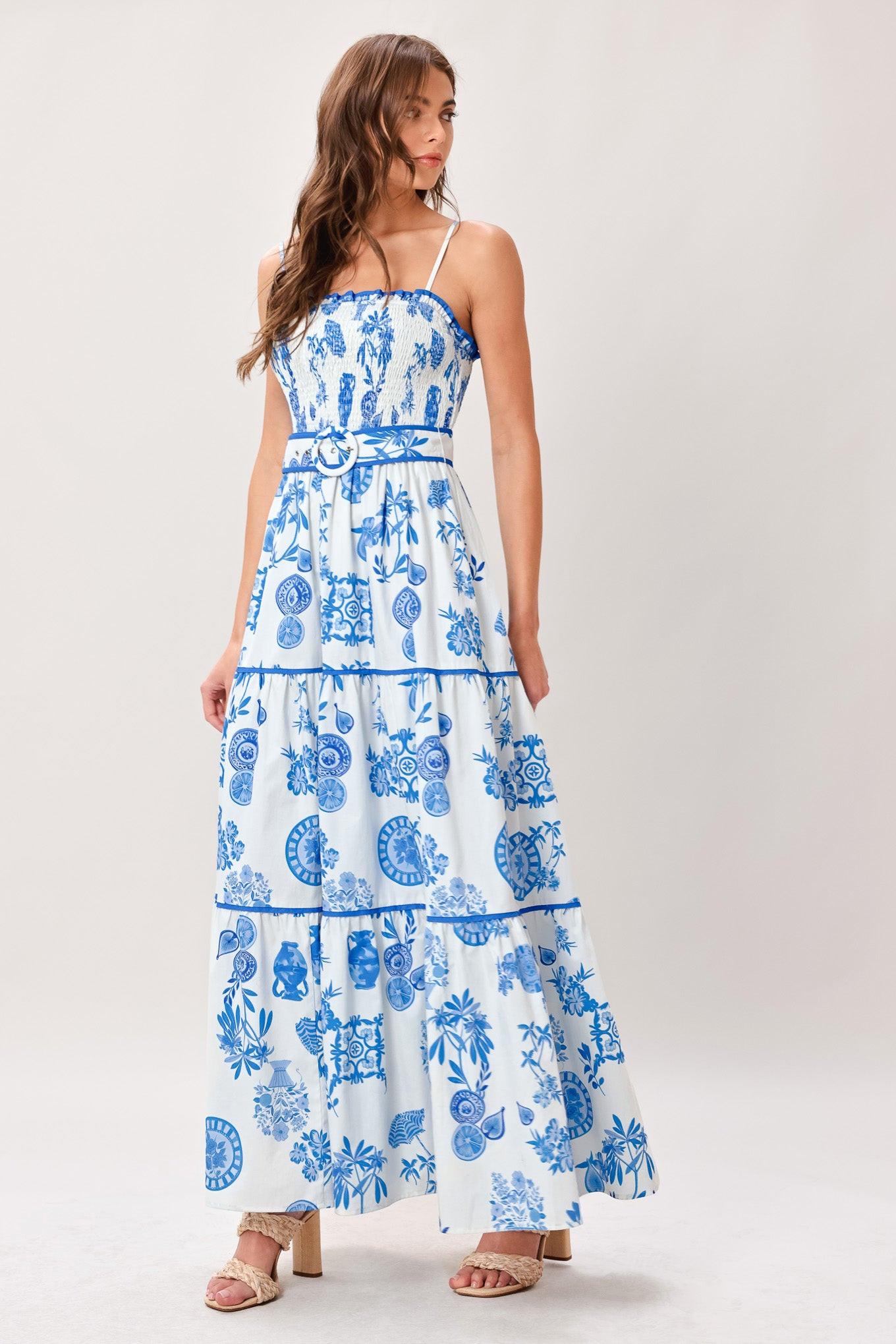 Woman wearing a blue and white patterned printed woven maxi dress featuring smocked bodice, straps, self belt and tier skirt