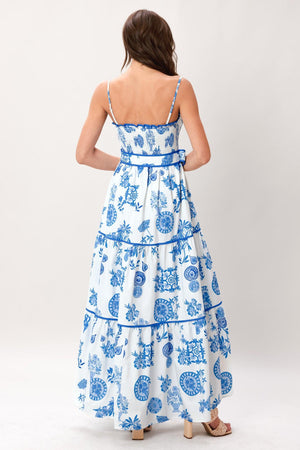 Woman wearing a blue and white patterned printed woven maxi dress featuring smocked bodice, straps, self belt and tier skirt