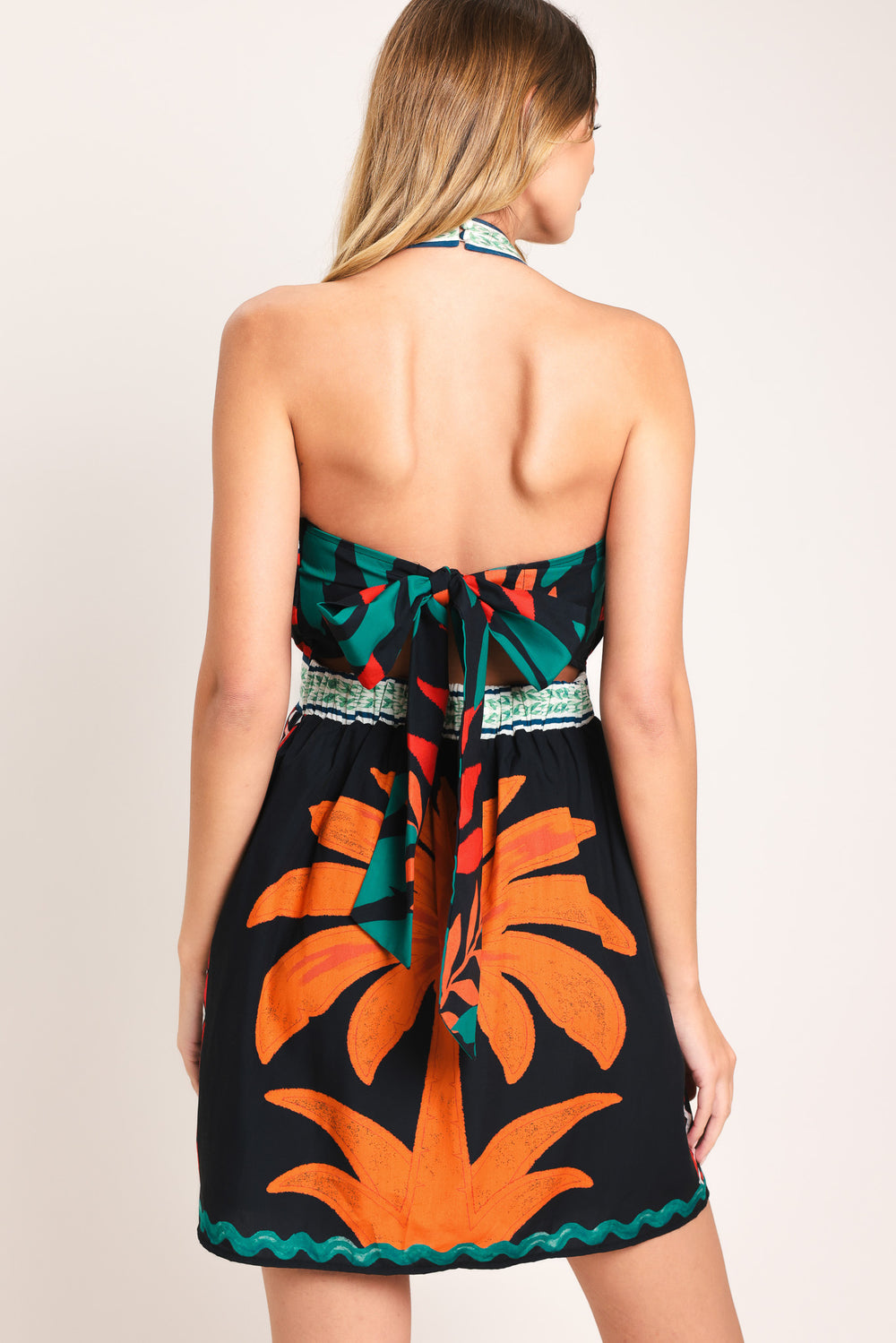 Woman wearing a colorful mini dress with palm tree design featuring twist halter neckline, smocked back waist band and back tie | Flying Tomato