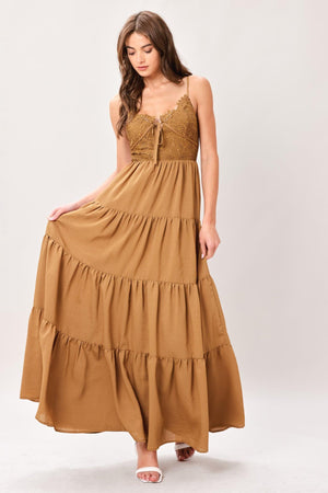 Woman wearing a brown tiered solid woven maxi dress featuring lace bodice with front tie, straps, tier skirt and smocked back bodice