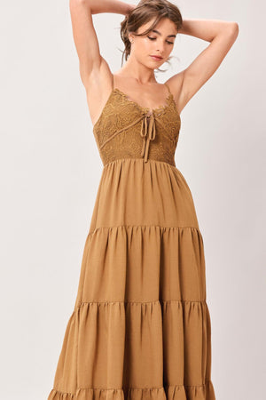 Woman wearing a brown tiered solid woven maxi dress featuring lace bodice with front tie, straps, tier skirt and smocked back bodice