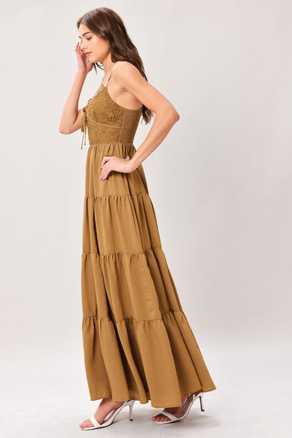 Woman wearing a brown tiered solid woven maxi dress featuring lace bodice with front tie, straps, tier skirt and smocked back bodice