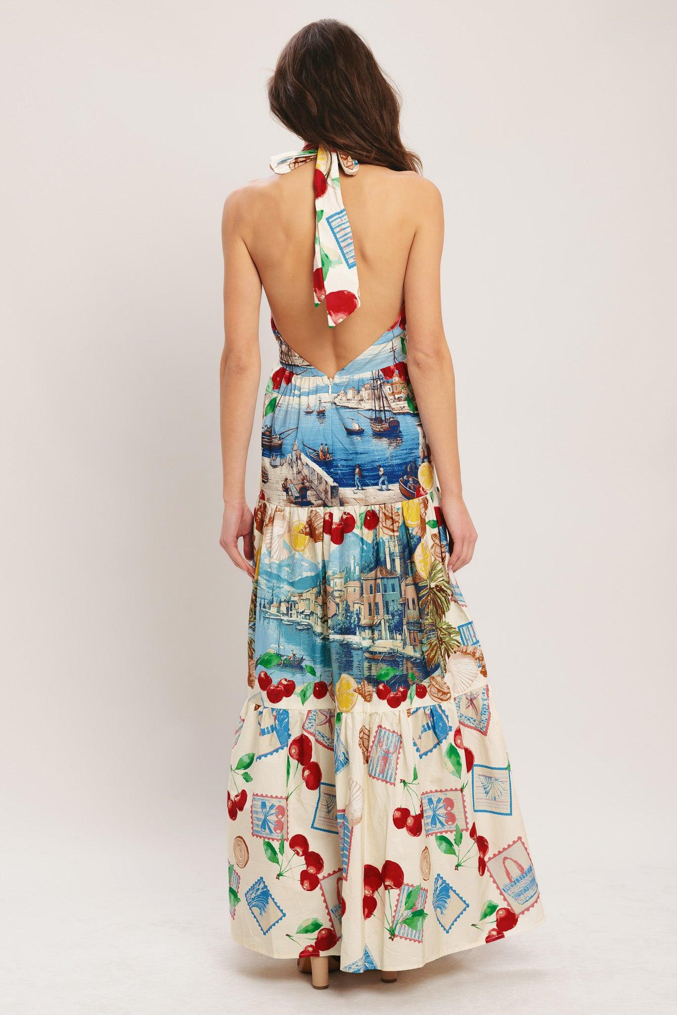 Woman wearing a colorful dress with a pattern of cherries and boats on a plain background