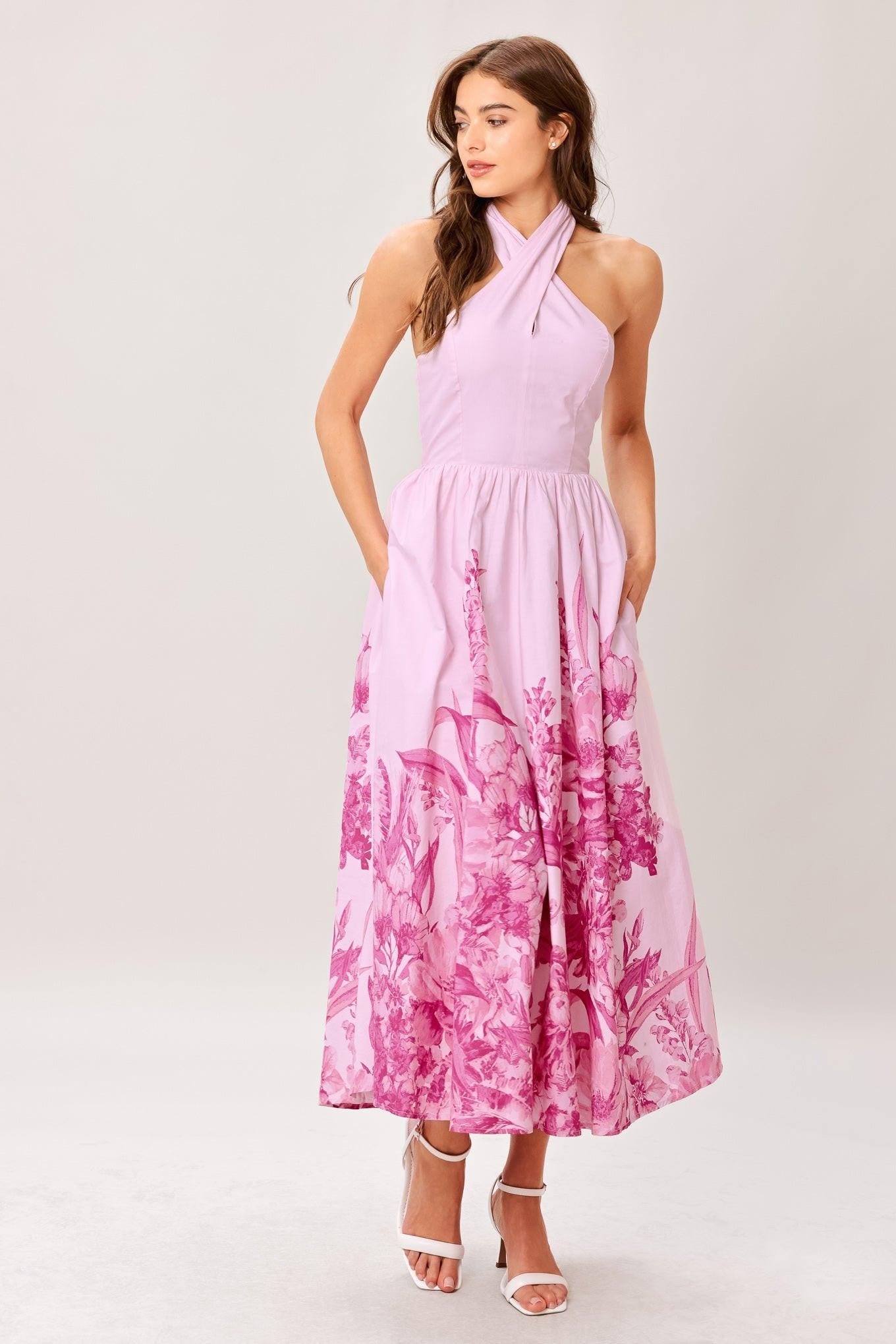 Woman wearing a pink floral printed woven midi dress featuring twist front with back neck tie, full skirt and smocked back bodice