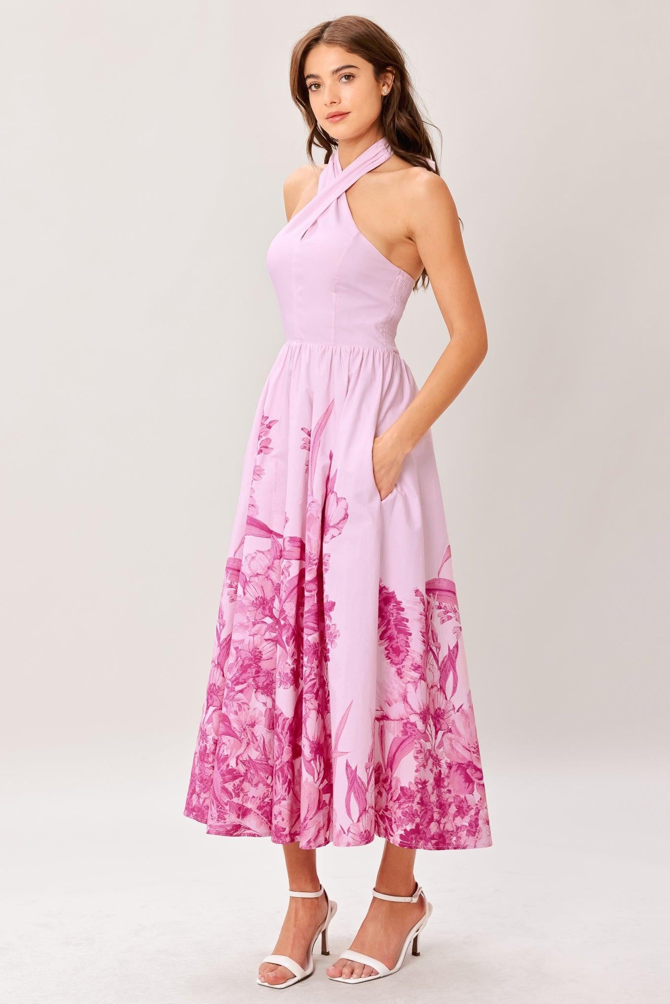 Woman wearing a pink floral printed woven midi dress featuring twist front with back neck tie, full skirt and smocked back bodice